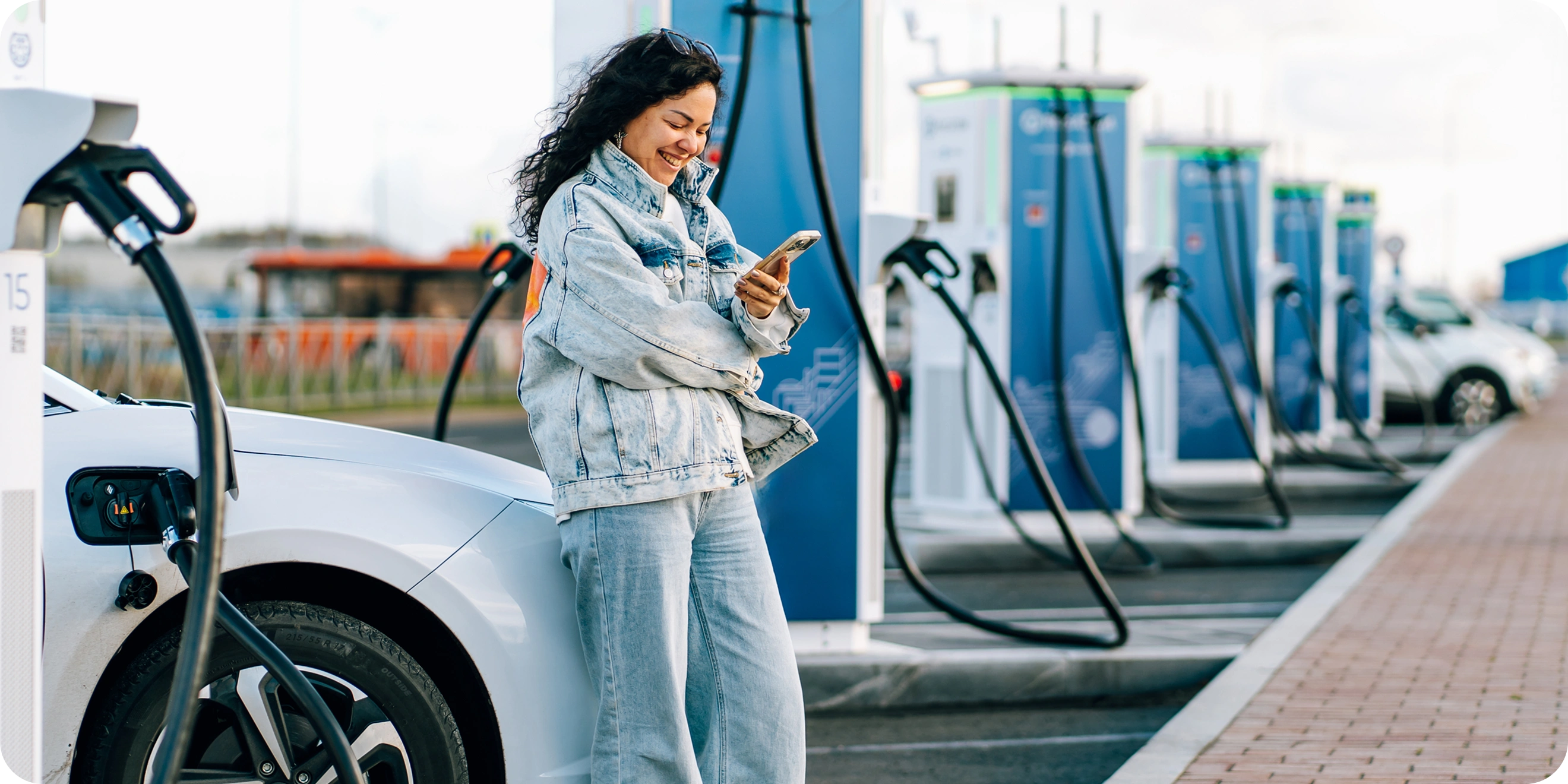 Zákazník čaká pri nabíjačke elektromobilu a platí cez mobilnú aplikáciu v telefóne.
