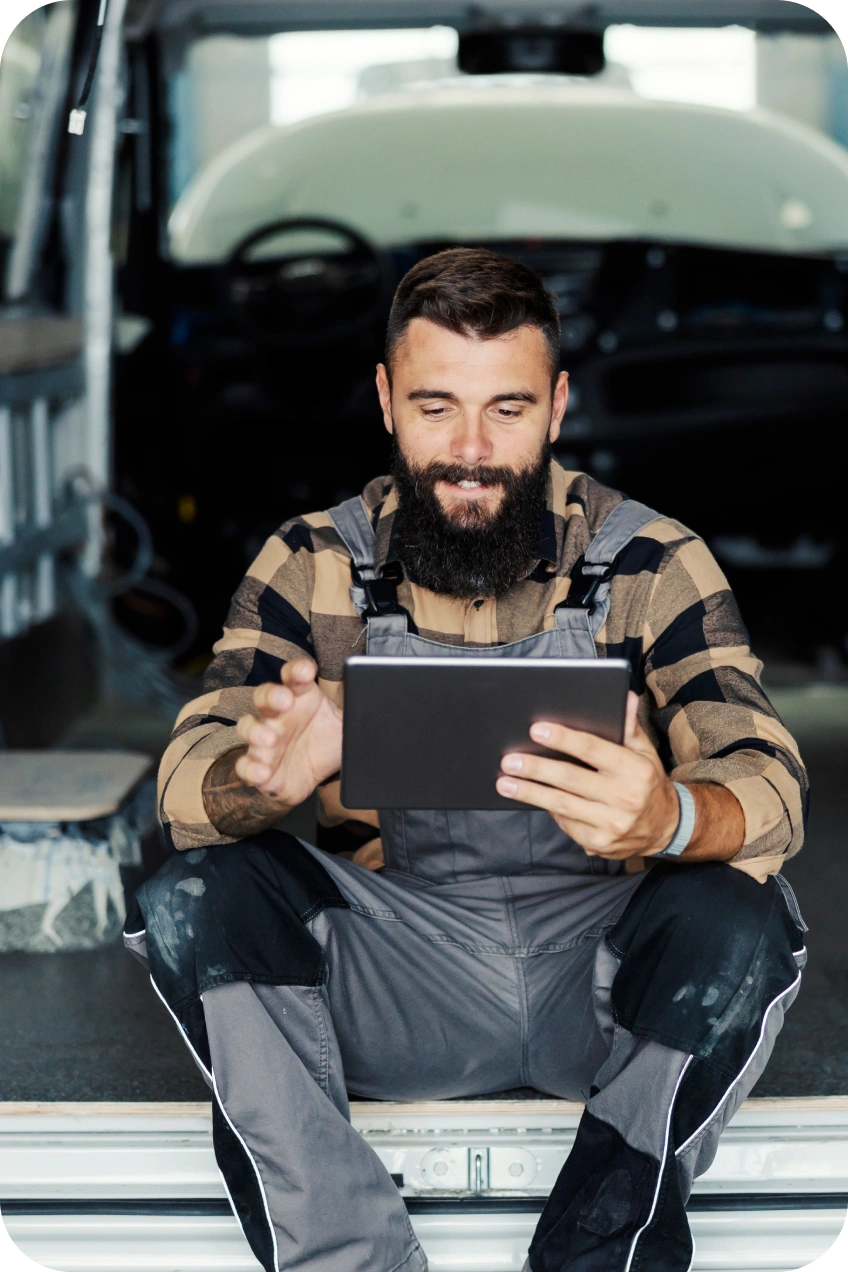 Automechanik sedí v dielni a používa tablet.