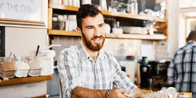Barista podáva zákazníkovi platobný terminál pri pulte v kaviarni.